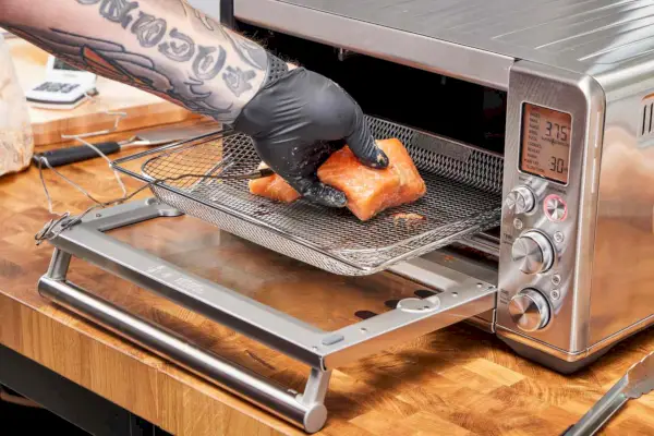 Une main plaçant le saumon sur une grille en direction de la friteuse à air Breville the Smart Oven
