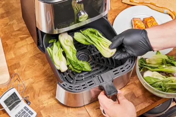 Une main gantée ajoutant des légumes dans la friteuse à air Instant Vortex Plus 6QT XL