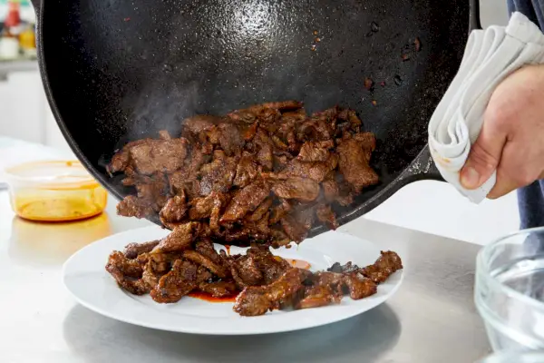 Osoba nalewająca jedzenie z Lodge Bold Cast Iron Wok na talerz