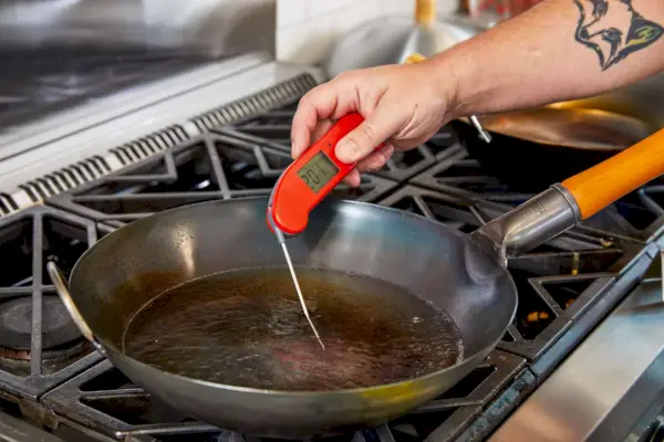 Osoba sprawdzająca temperaturę cieczy w patelni Yosukata Carbon Steel Wok za pomocą termometru