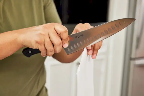 ידיים פורסות פיסת נייר עם Mac Knife 8-Inch Hollow Edge Chef