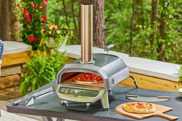 Gotowana pizza na drewnianej skórce przed gazowym piecem do pizzy Ooni Koda 16 ustawionym na zewnątrz