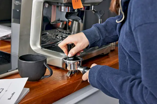 Person drückt gemahlene Espressobohnen in den Siebträger einer Breville Barista Pro Espressomaschine