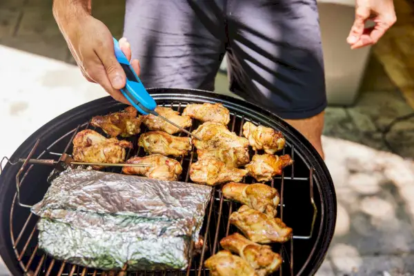 אדם בודק את הטמפרטורה על בשר מבושל ב- Weber Smokey Mountain Cooker 18-Inch Charcoal Smoker (721001)