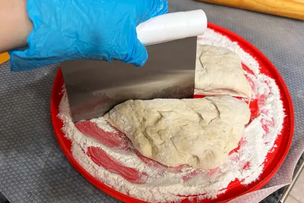 Une personne utilise le grattoir d'établi 3 en 1 Chefn Pastrio pour couper la pâte