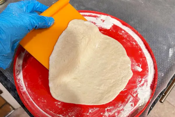 Une personne utilise le grattoir d'établi 3 en 1 Chefn Pastrio pour ramasser la pâte
