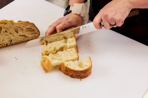 אדם משתמש בסכין משוננת סט קאנגשאן מאיה בלוק 12 חלקים כדי לחתוך לחם