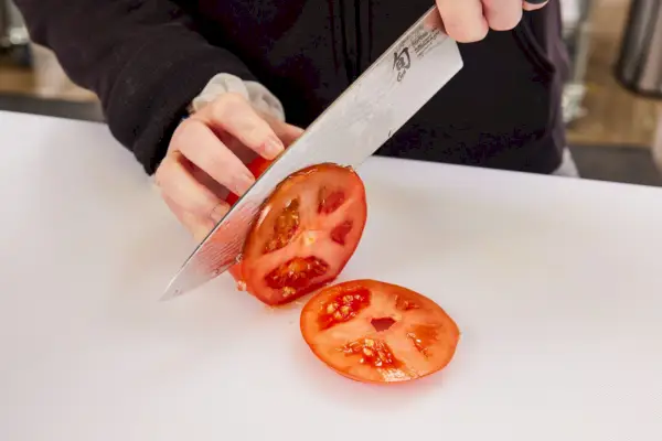 אדם חותך עגבנייה בסכין מסט בלוק סכין קלאסי של Shun של 9