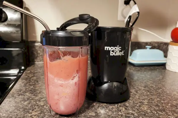 Základňa, šálka a veko Magic Bullet 11-dielnej súpravy mixéra na kuchynskej linke s ružovým smoothie v šálke