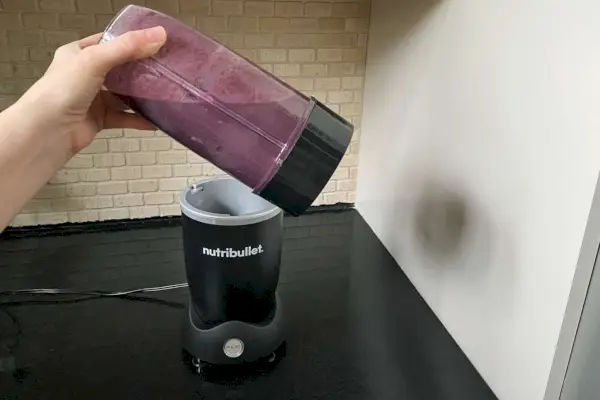 Ruka drží pohár Nutribullet Pro+ Personal Blender s fialovým smoothie vo vnútri