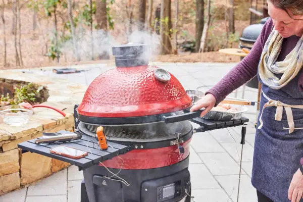 Osoba podnosi górę 18-calowego cyfrowego grilla węglowego i wędzarni Kamado Joe Konneted Joe
