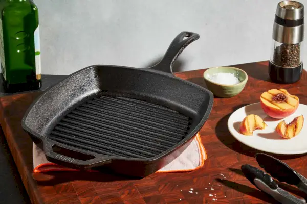 Die gewürzte quadratische Grillpfanne aus Gusseisen von Lodge auf einem Tisch neben einem gegrillten Pfirsich.