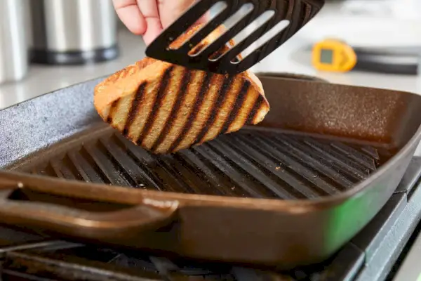 Nahaufnahme von jemandem, der ein gegrilltes Käsesandwich in der Grillpfanne Nr. 12 von Smithey Ironware Co. umdreht.