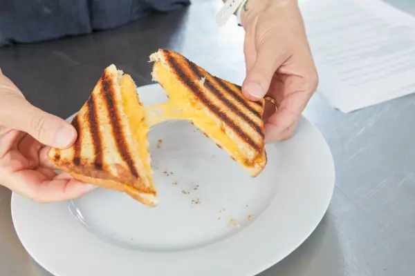 Eine Person zeigt, wie geschmolzen der Käse eines gegrillten Käsesandwichs ist.