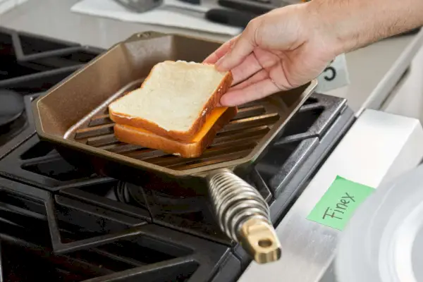 Eine Person legt die oberste Brotscheibe auf ein Sandwich, das in der 10-Zoll-Gusseisen-Grillpfanne von Finex gegrillt wird.