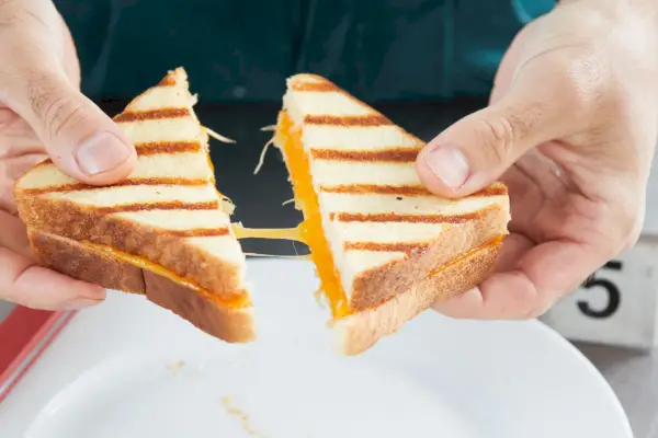 Eine Person hält einen geschnittenen Grillkäse in der Hand, um den geschmolzenen Käse darin zu zeigen.