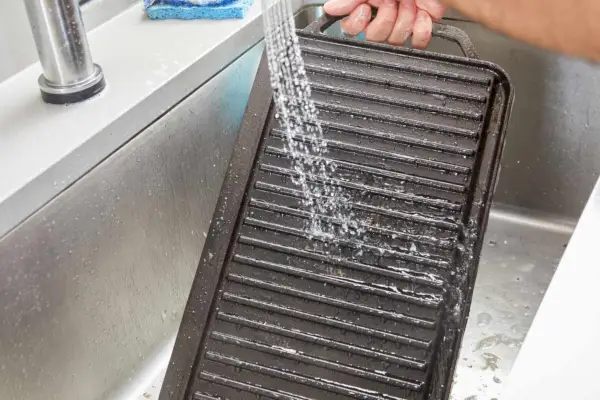 Eine Person lässt Wasser auf den umkehrbaren Gusseisengrill/Grill von Lodge laufen.