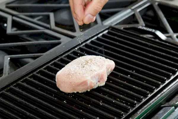 Eine Person salzt ein Schweinekotelett, während es auf dem umkehrbaren Gusseisengrill/Grill von Lodge gegart wird.