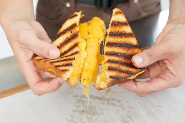 Eine Person spaltet einen gekochten Grillkäse auf, um den geschmolzenen Käse darin zu sehen.