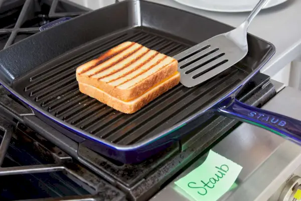 Eine Person dreht einen gegrillten Käse um, der in der emaillierten Gusseisen-Grillpfanne von Staub gegart wird.