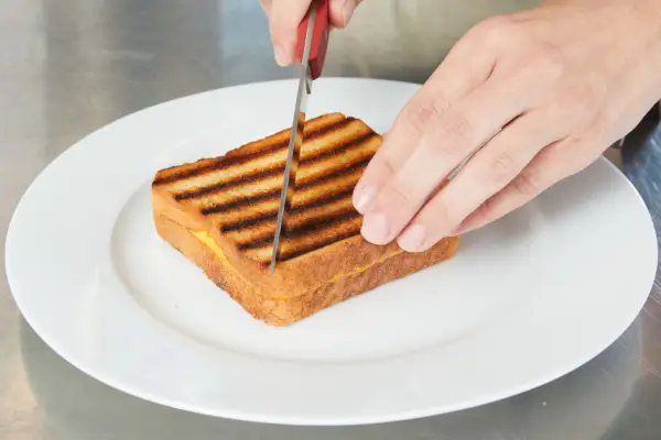 Eine Person schneidet einen gegrillten Käse in zwei Hälften.