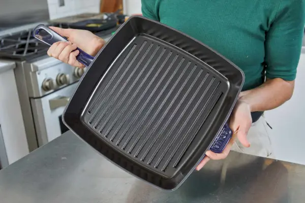 Eine Person hält die emaillierte Gusseisen-Grillpfanne von Staub hoch.