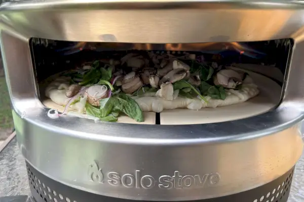 Domowa pizza z grzybami, cebulą, szpinakiem i serem piecze się w oświetlonym piecu do pizzy Solo Stove Pi Prime.