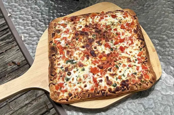 Upieczona mrożona pizza leży na drewnianej skórce pizzy.