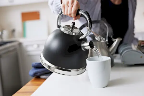 Persona che versa l'acqua dal bollitore per il tè con fischio Susteas Stove Top in una tazza