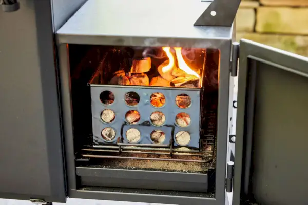 אדם מניח שבבי עץ ב-Dyna-Glo Wide Body Vertical Offset Charcoal Smoker (DGO1890BDC-D)
