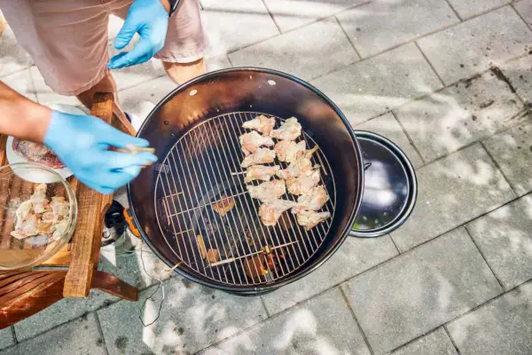 אדם מניח עוף נא בתוך החבילה הקלאסית Pit Barrel Cooker - 18.5 אינץ' תוף מעשן