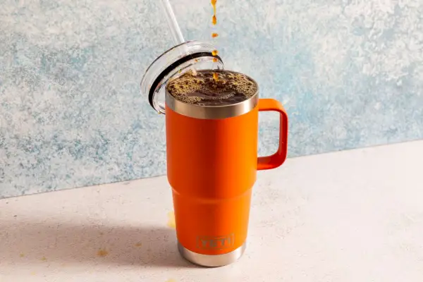 Kaffee tropft in einen Yeti-Becher auf einer Arbeitsplatte mit blau-weißem Tapetenhintergrund