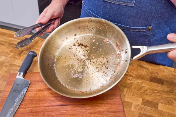 Osoba merajúca pravítkom 10-palcovú nerezovú panvicu na varenie Made in Cookware