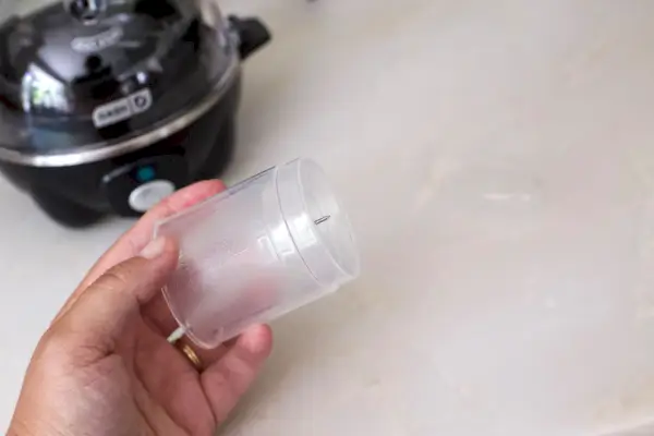 Osoba držící nádobu, která je dodávána s Dash Rapid Egg Cooker