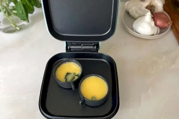 Dash Deluxe Egg Bite Maker s otevřeným víkem sedící na kuchyňské lince a vaření omelet
