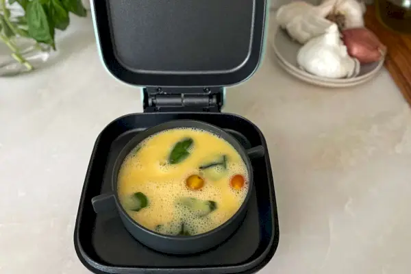 Dash Deluxe Egg Bite Maker s otevřeným víkem sedí na kuchyňské lince a vaří omeletu