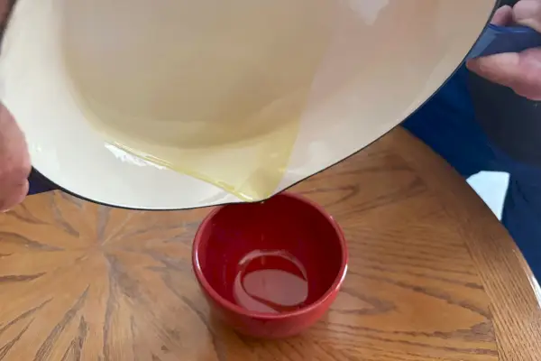 Zwei Hände gießen Öl aus der Lava-Gusseisen-Keramikpfanne mit emailliertem Gusseisen und seitlichen Tropfausläufen in eine Tasse
