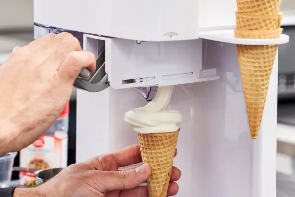Osoba, ktorá plní cukrový kornútok zmrzlinou z výrobníka zmrzliny Cuisinart Soft Serve