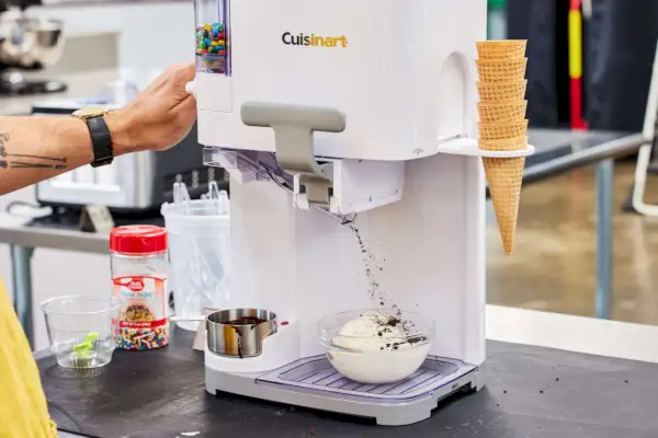 Osoba, ktorá vydáva polevy z výrobníka zmrzliny Cuisinart Soft Serve na sklenenú misku so zmrzlinou
