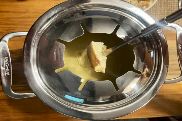 Chlieb je ponorený do syra vo vnútri celoobaleného liateho hliníkového fondue nádoby