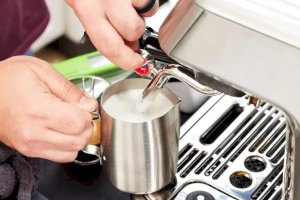 Uma pessoa usando o espumante de leite acoplado ao Breville The Barista Touch Impress (BES881BSS1BNA1)