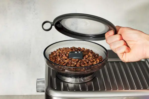 Close de uma pessoa segurando a tampa do moedor de café Breville The Barista Touch Impress (BES881BSS1BNA1)