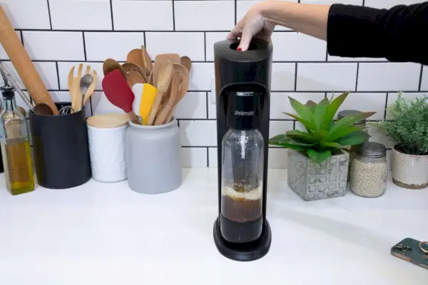 Osoba stlačí tlačidlo na zariadení na výrobu perlivej vody a sódy Drinkmate OmniFizz