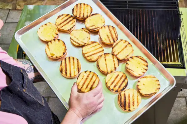 Uma pessoa remove pães de hambúrguer da churrasqueira a gás propano líquido de aço inoxidável com 3 queimadores Sabre Select