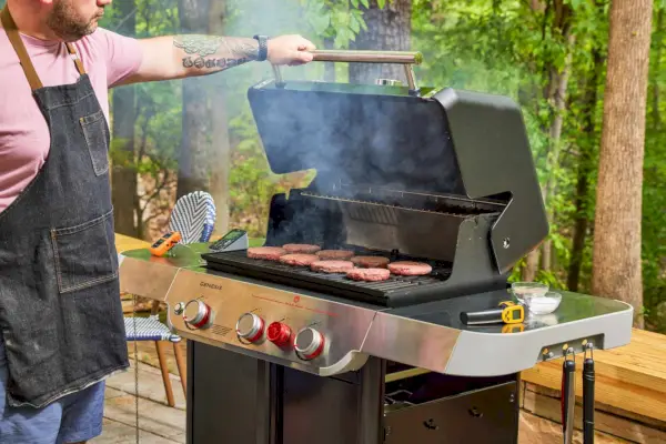 Uma pessoa levanta a tampa da churrasqueira a gás propano líquido Weber Genesis E-325