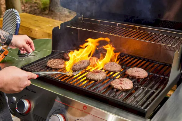 Uma pessoa cozinha carne na churrasqueira a gás propano líquido Weber Genesis E-325