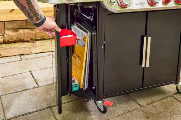 Uma pessoa abre uma porta na lateral da churrasqueira a gás Weber Genesis E-335