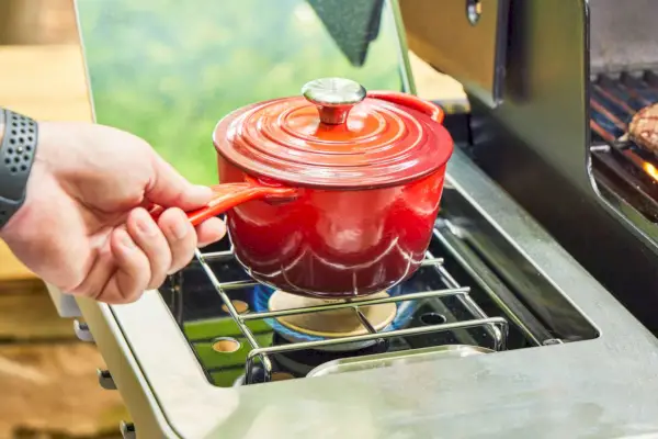 Uma pessoa cozinha comida em uma panela pequena ao lado da churrasqueira a gás Weber Genesis E-335