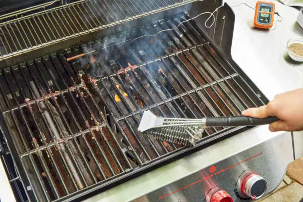 Uma pessoa limpa a churrasqueira a gás Weber Genesis E-335 com uma escova para grelhar