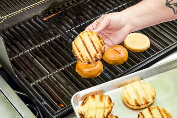 Uma pessoa remove pães de hambúrguer da churrasqueira a gás Weber Genesis E-335
